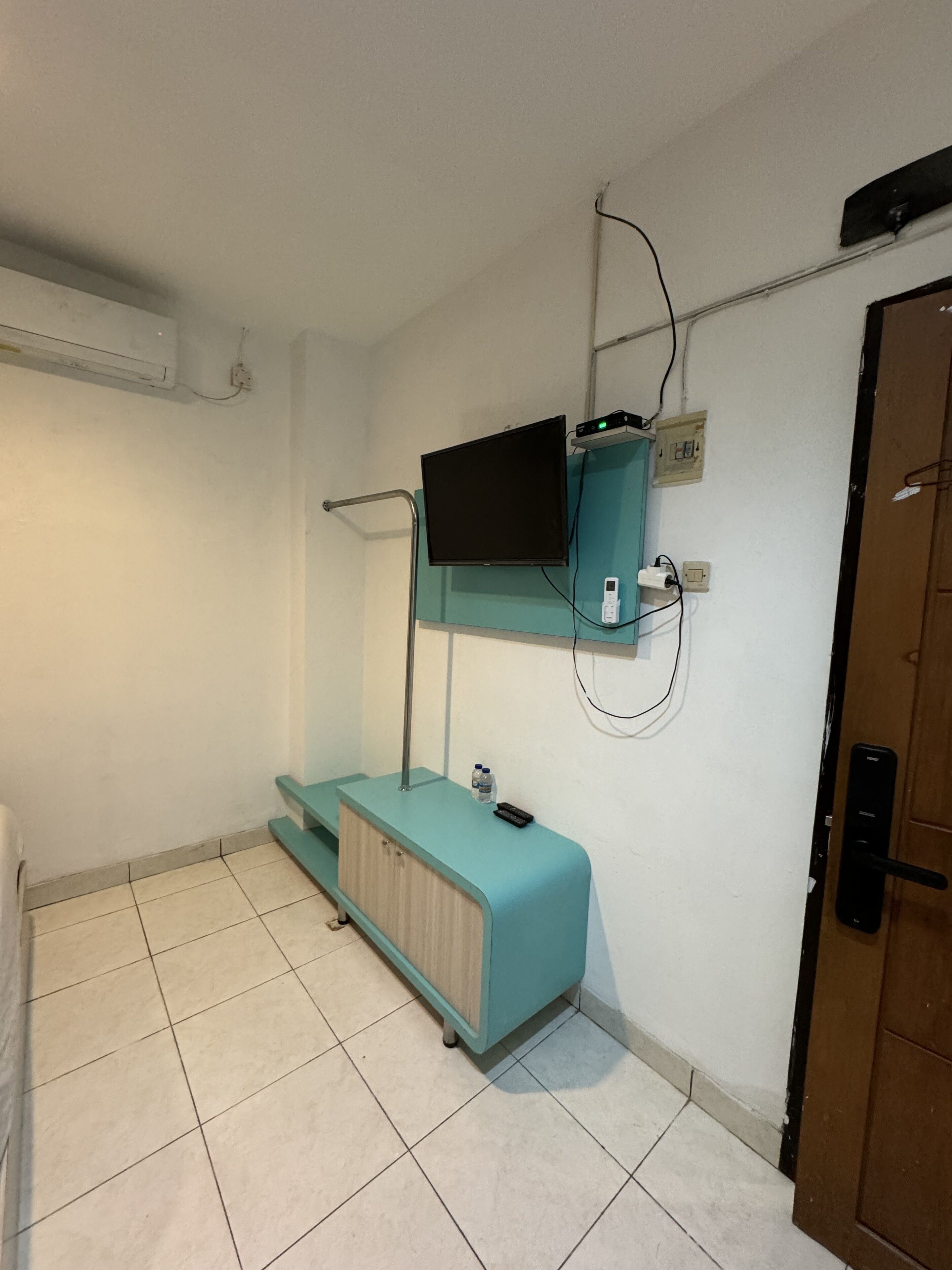 Una habitación pequeña y limpia con un mueble color turquesa, un televisor montado y una puerta con picaporte.