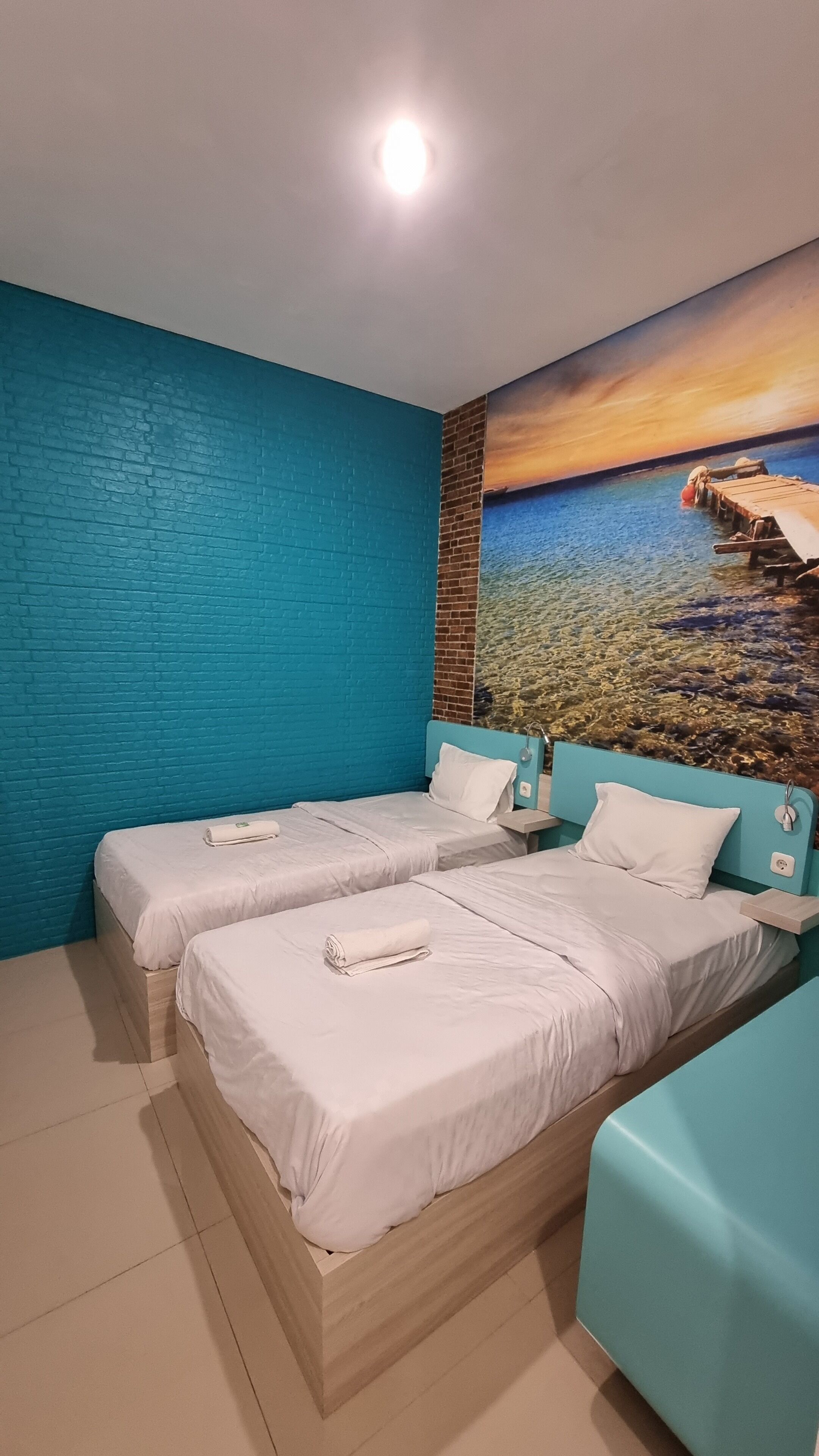 Una habitación con dos camas, un mural de una puesta de sol sobre el agua y una pared de ladrillo azul.