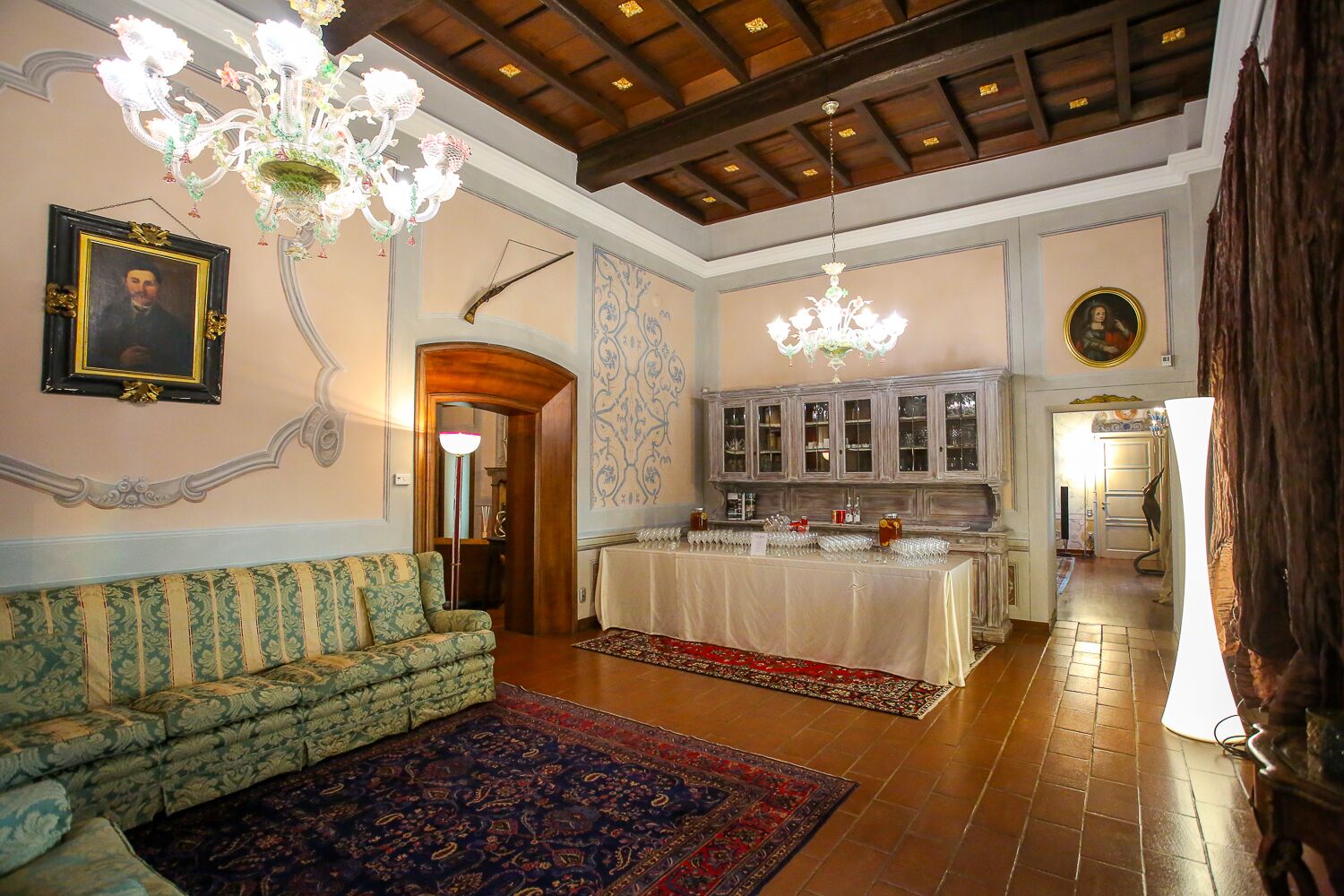 Ein geräumiges Zimmer mit einem grün gemusterten Sofa, einer Essecke mit Tisch und gedecktem Tisch für eine Mahlzeit sowie einem Kronleuchter.