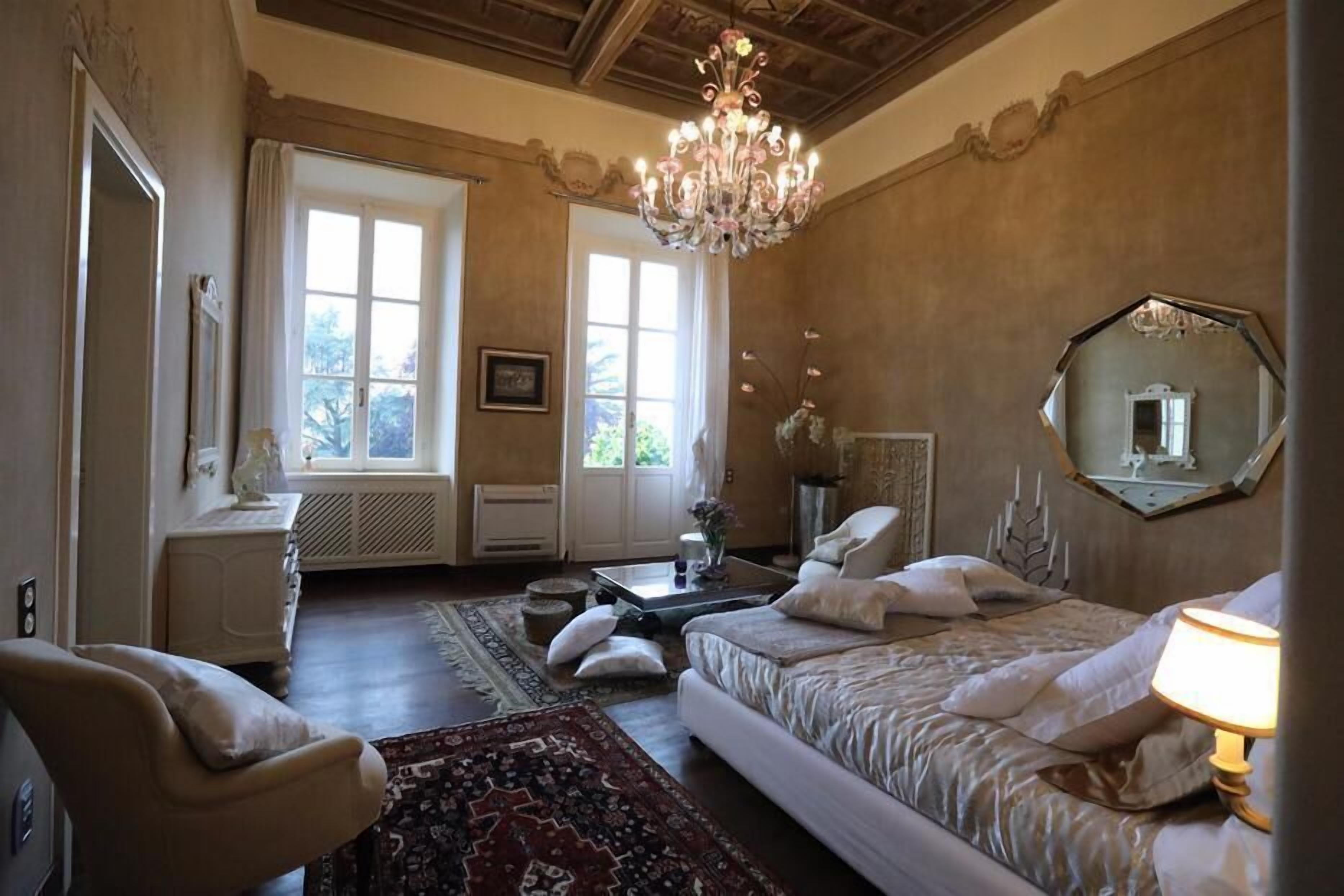 Una camera da letto con un letto grande, un'area salotto con una poltrona, un lampadario e un ampio specchio a parete.