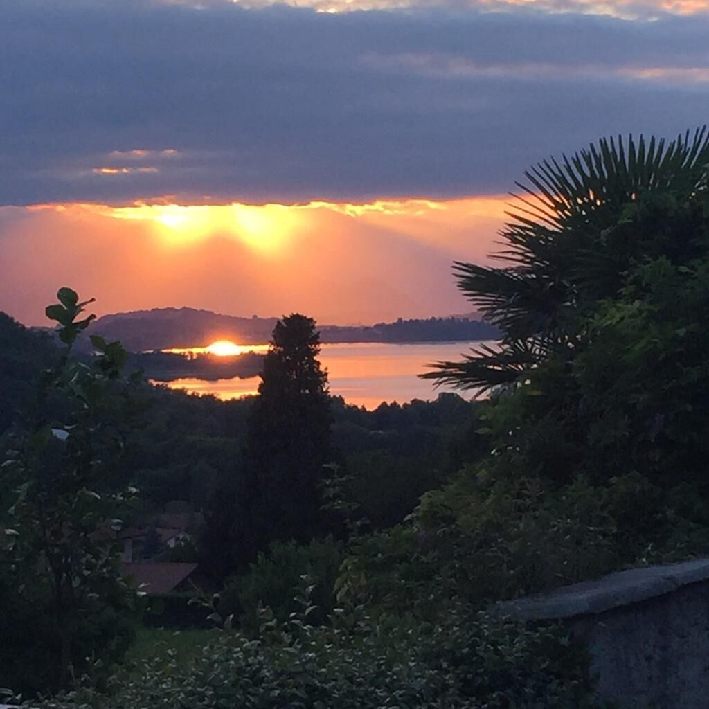 A sunset over a lake with surrounding greenery and a distant mountain.