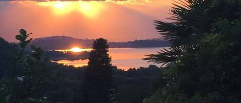 A sunset over a lake with surrounding greenery and a distant mountain.