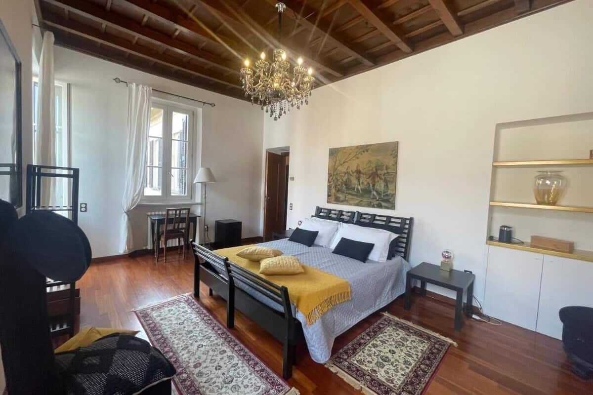 A bedroom with a large bed, a chandelier, a desk, and a chair.
