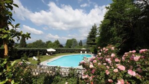 A swimming pool surrounded by lush greenery and pink flowers. - Villa Ghiringhelli (Azzate)
