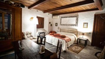 Une chambre confortable avec un plafond en bois, un lit doté d’une tête de lit blanche, une petite table avec des chaises et un tapis sur le sol.