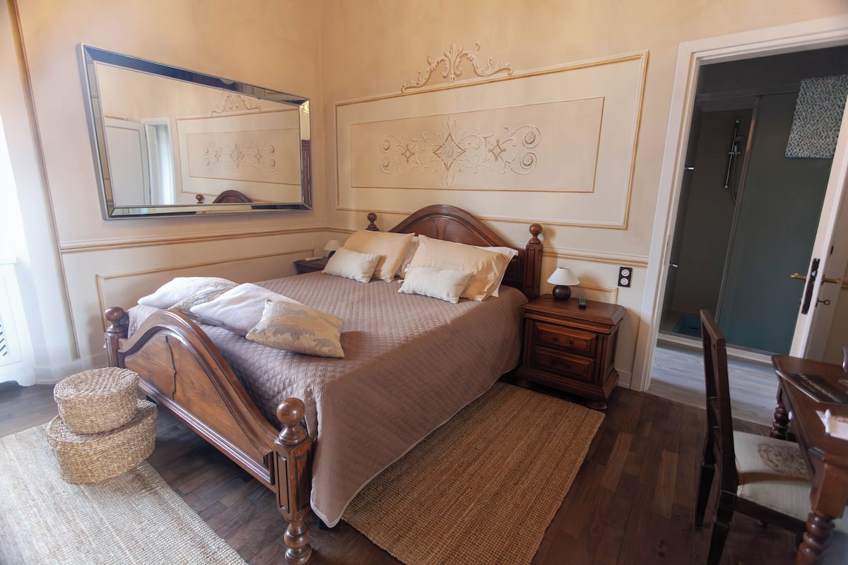A bedroom with a wooden bed, a nightstand, a mirror, and a door leading to a bathroom.