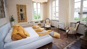 A bedroom with a large bed, two armchairs, a small table, and a mirror. - Villa Ghiringhelli (Azzate)
