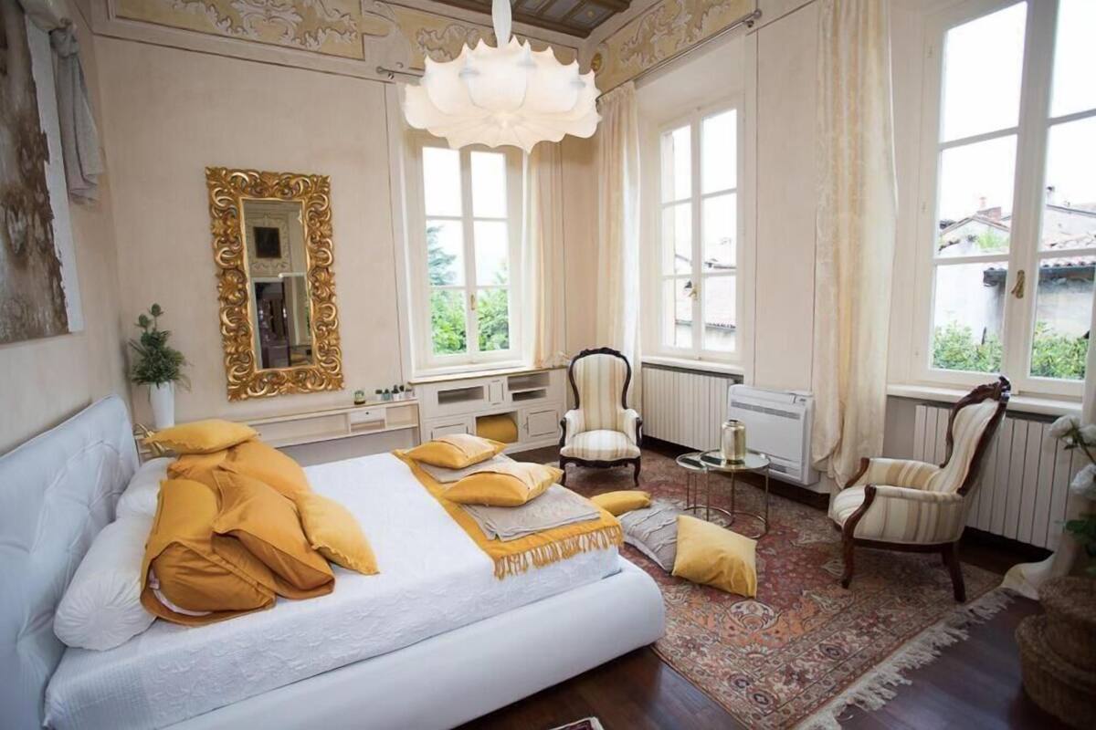 A bedroom with a large bed, two armchairs, a small table, and a mirror.