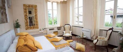 Un dormitorio con una cama grande, dos sillones, una mesita y un espejo.