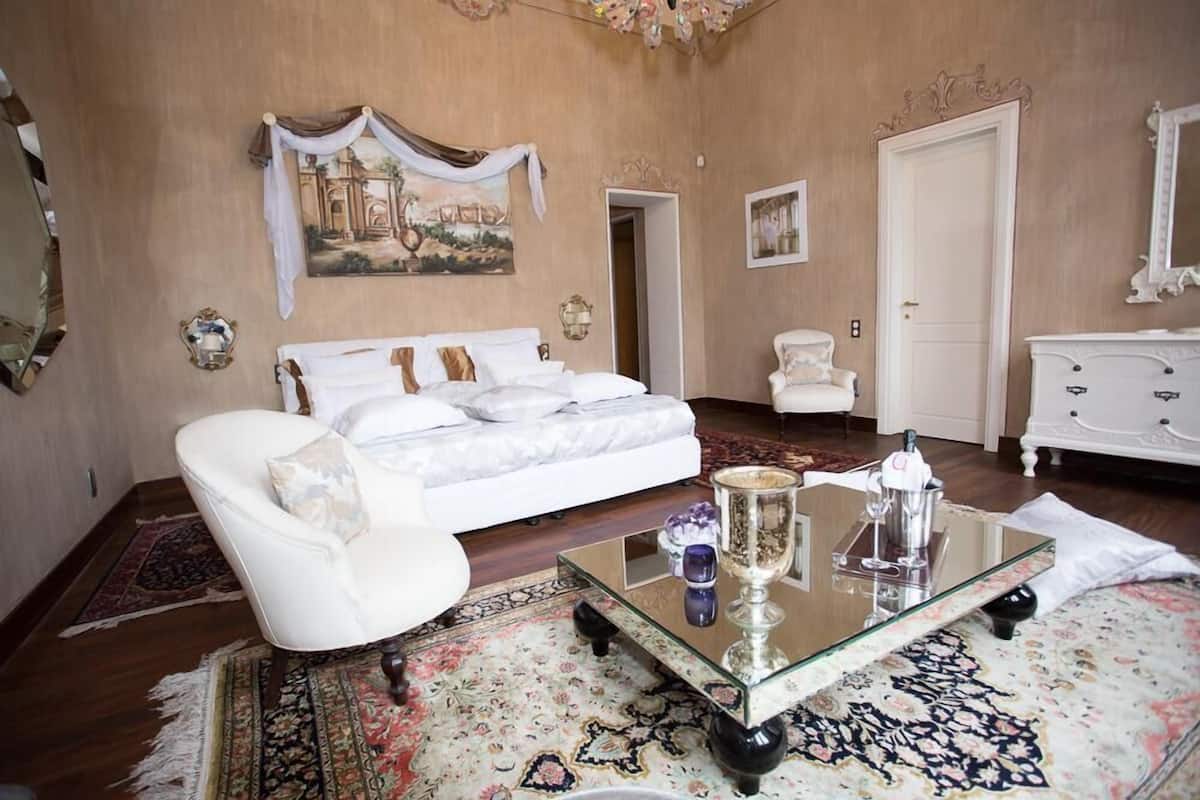 A spacious bedroom with a large bed, a sitting area with a glass coffee table, and a classic white dresser.