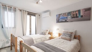 Une chambre avec deux lits, une fenêtre avec des rideaux légers, un appareil de climatisation et un tableau représentant une voiture accroché au mur.