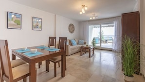 Un salon moderne avec un coin repas, comprenant un canapé, une table à manger avec des chaises, une horloge et une grande fenêtre offrant une vue dégagée.
