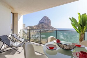 Een balkon met een tafel voor twee, met uitzicht op de kust en een opvallende rotsformatie.