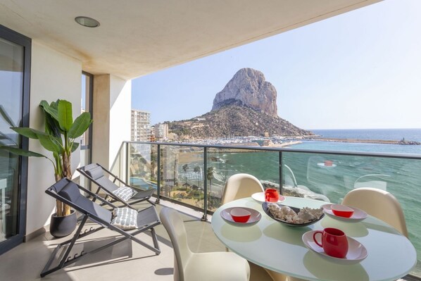 Een balkon met een tafel voor twee, met uitzicht op een strand en een berg.