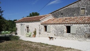 A stone building with a tiled roof, a gravel driveway, and a dog in the foreground.
