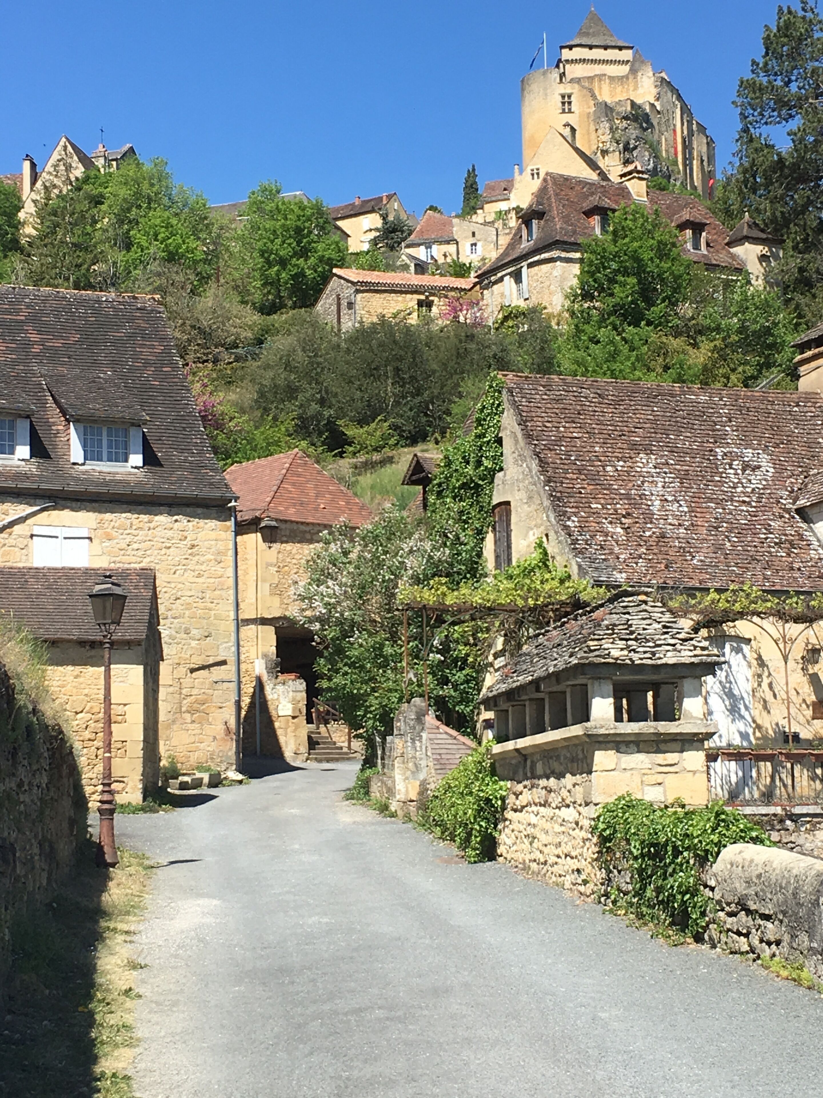 Una calle estrecha en un pueblo histórico con edificios de piedra, una iglesia y un castillo al fondo.