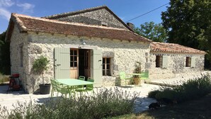A stone house with a tiled roof, a small garden, and a table with chairs.