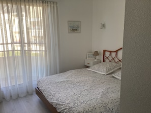 A bedroom with a bed, a nightstand, a lamp, a picture on the wall, and sheer curtains.