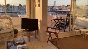 A balcony with a TV, seating, and a view of a marina with boats. - Ile aux Moines (Arzon)