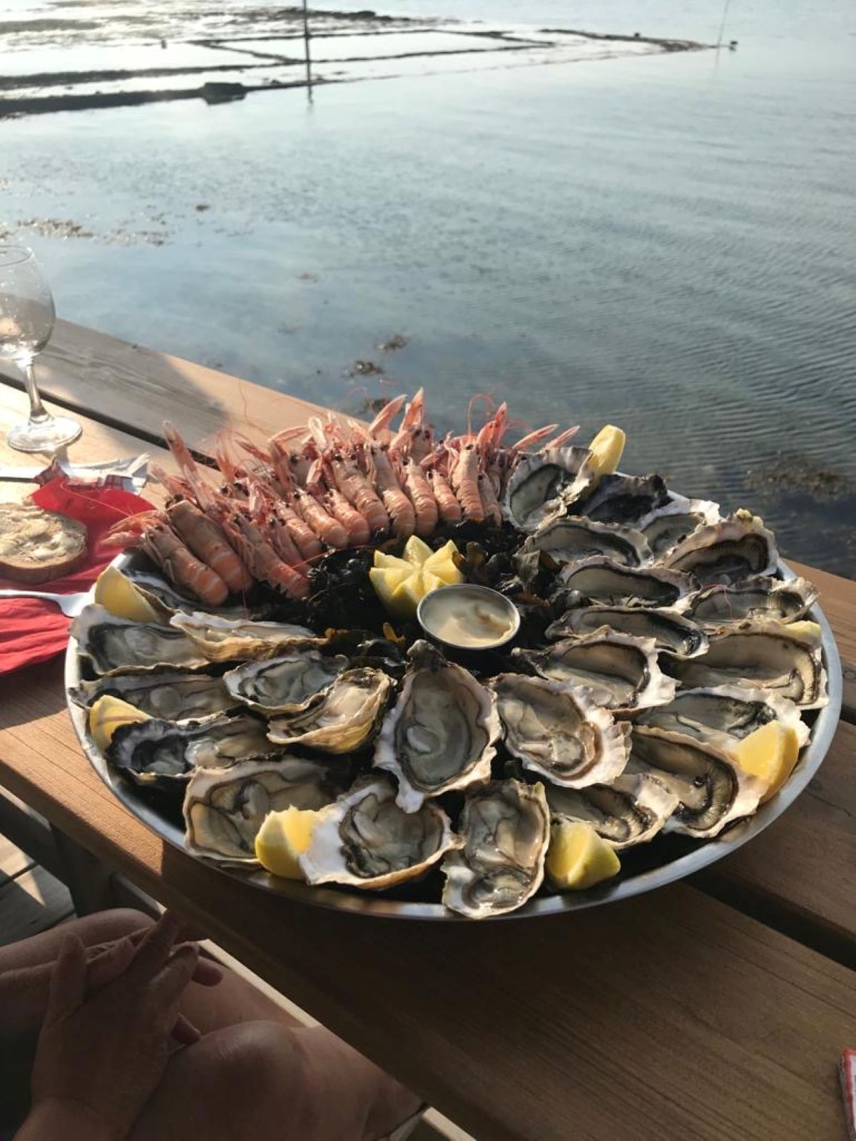 Una bandeja de mariscos con ostras y camarones sobre una mesa de madera cerca del agua.