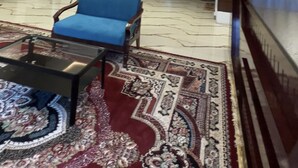 Un vestíbulo moderno con un sofá azul, una mesa de centro de vidrio, un tapete estampado, una araña y un mostrador de recepción.