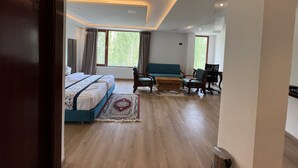 Habitación de hotel moderna con una cama grande, un sofá, un escritorio y vistas a zonas verdes.