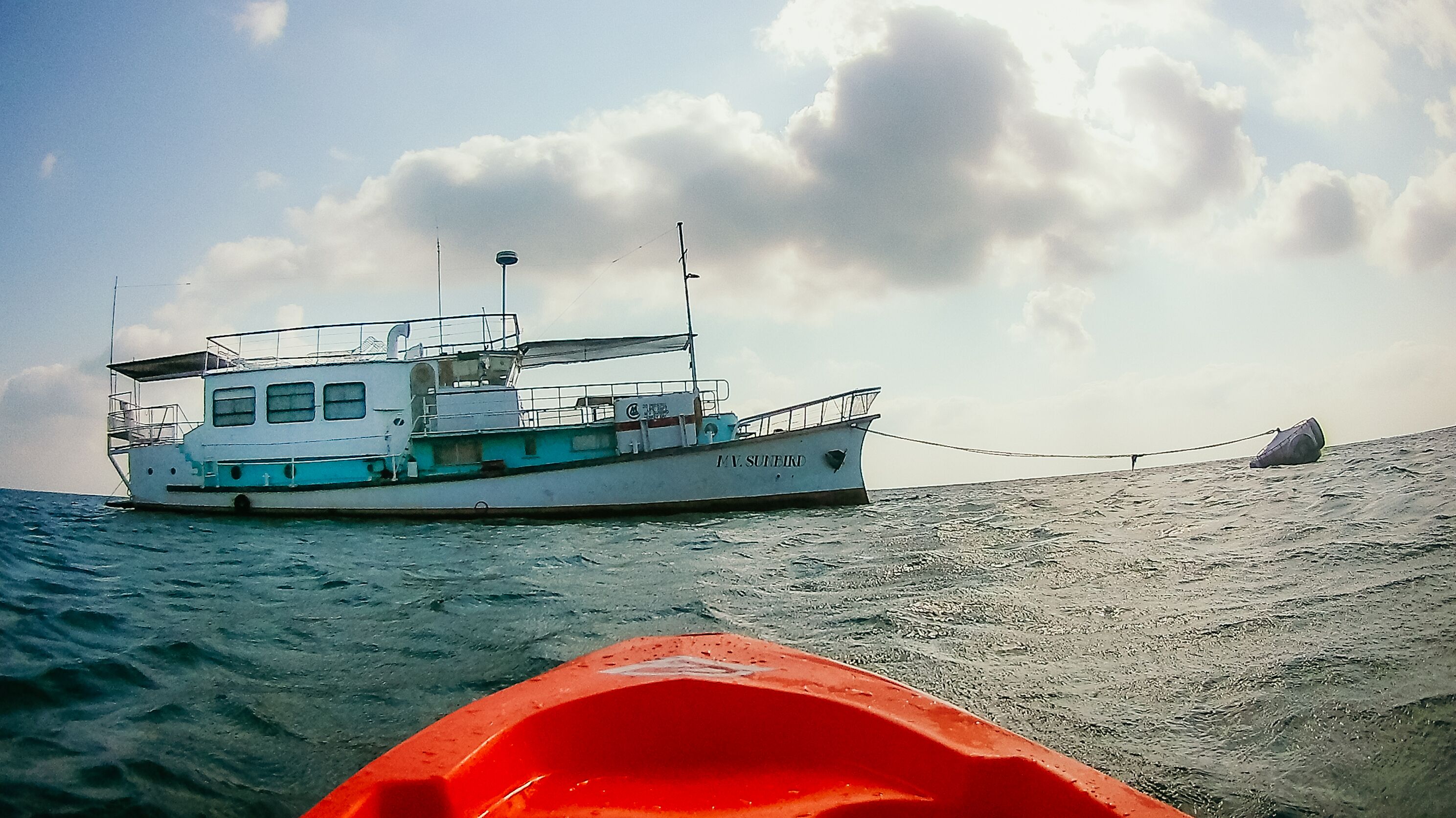 A boat named 'T.V. Sunfield' anchored near a sandy shore with a clear sky.