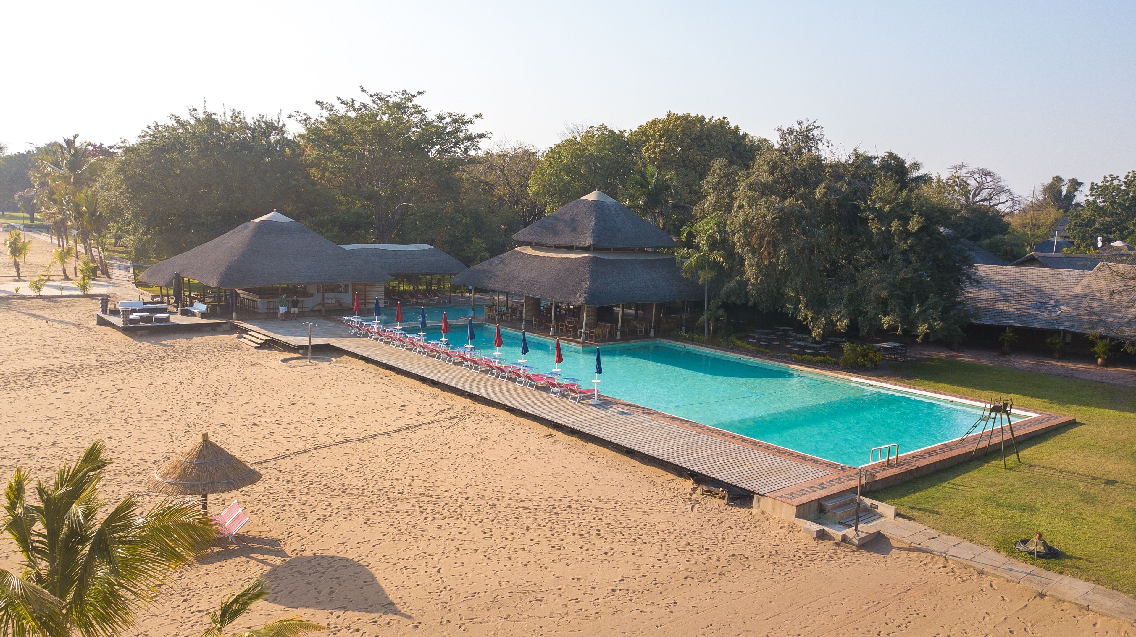 Een resort met een groot zwembad, ligbedden en bungalows met rieten daken.