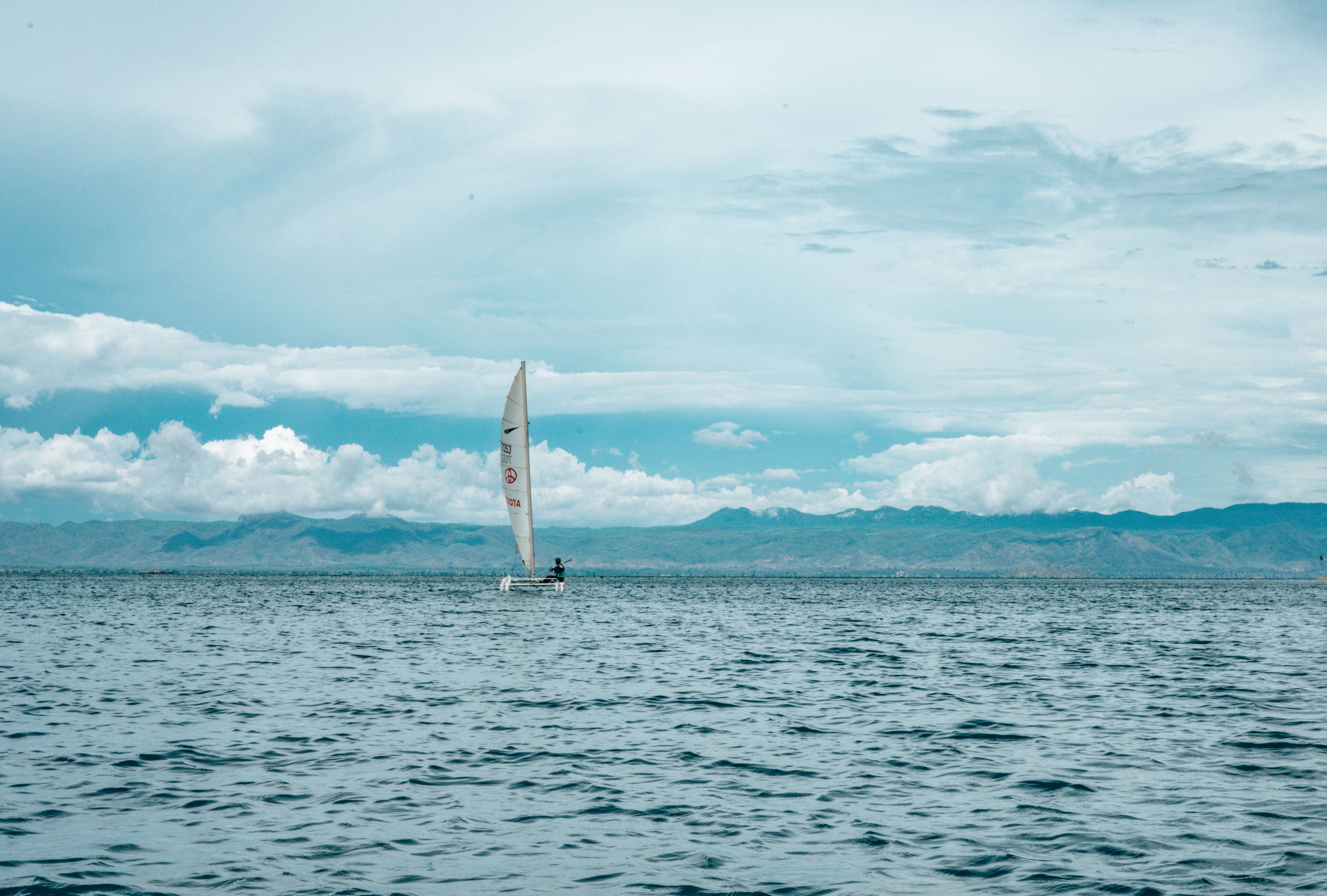 A sailboat on a calm body of water with mountains in the background.