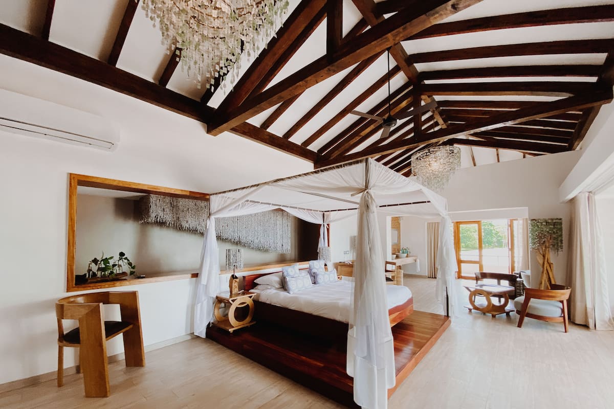 Een ruime slaapkamer met een hemelbed, houten balken, een baldakijn en een grote spiegel.
