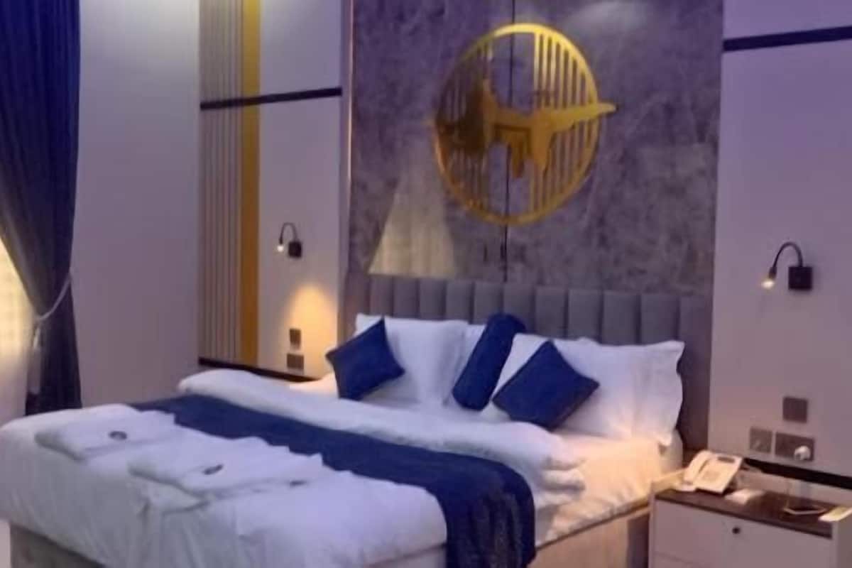 A modern hotel room with a large bed, a nightstand, a wall-mounted lamp, and a decorative ceiling light.