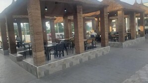 A covered outdoor seating area with tables and chairs, stone pillars, and a tiled floor. - Armed Forces Officers Mess & Suites (Abuja)