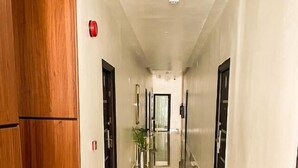 A corridor with a wooden door on the left, a plant in the center, and a door at the end. - Armed Forces Officers Mess & Suites (Abuja)