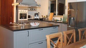Een moderne keuken met een groot eiland, roestvrijstalen apparatuur en houten stoelen.