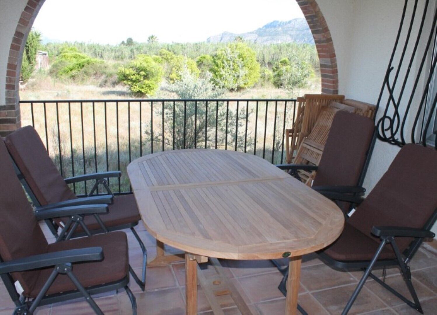 Um pátio com mesa de madeira e quatro cadeiras, parede de tijolos e vista para uma paisagem montanhosa.