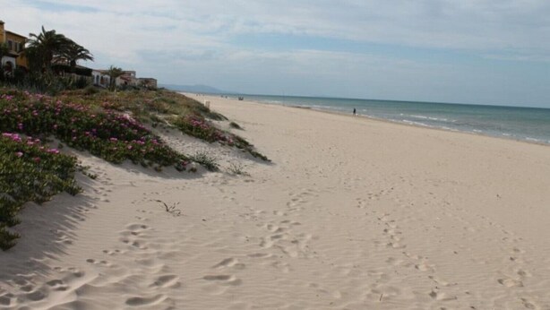 Een zandstrand met voetafdrukken, een heldere lucht en een verafgelegen uitzicht op de zee.