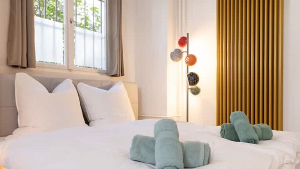 Ett hotellrum med en säng, kuddar, ett sängbord, en lampa och utsikt över omgivningarna.