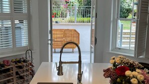 Une cuisine équipée d’un évier intégré, d’un meuble à vin et offrant une vue sur le jardin grâce à la porte ouverte.