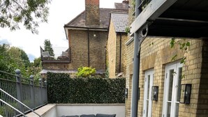 Un espace extérieur aménagé, abrité, avec un canapé et une table intégrés, une terrasse en bois et un bâtiment en briques doté d’une porte blanche.