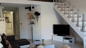 A modern living room with a white sofa, a round ottoman, a flat-screen TV, and a staircase with a metal railing. - Corse LES Pieds Dans L'eau (Borgo)
