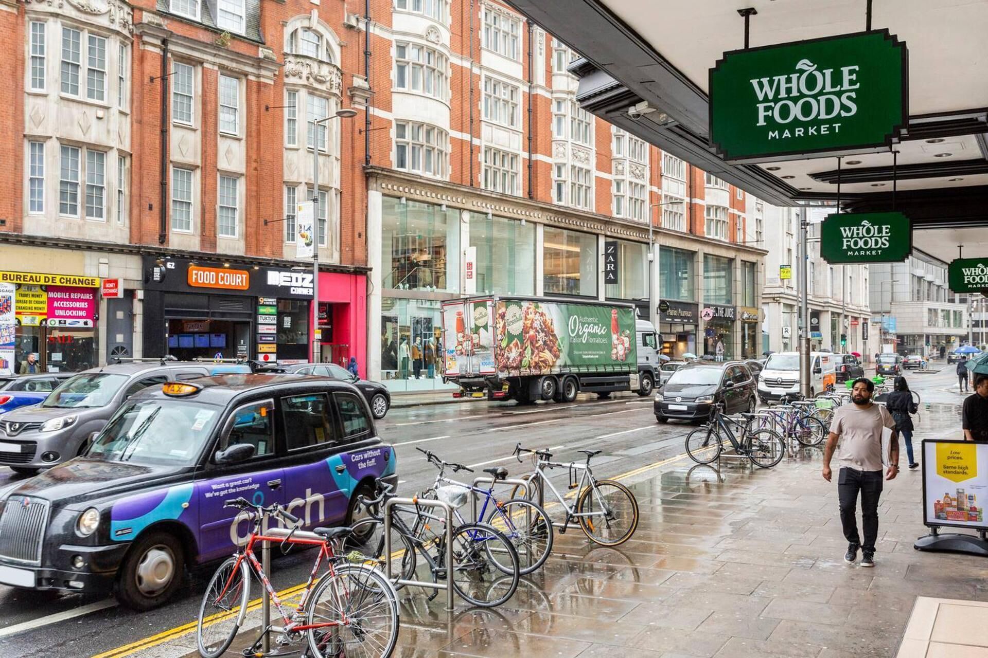 Eine belebte Straße mit einem Schild von Whole Foods Market, einem Taxi und abgestellten Fahrrädern.