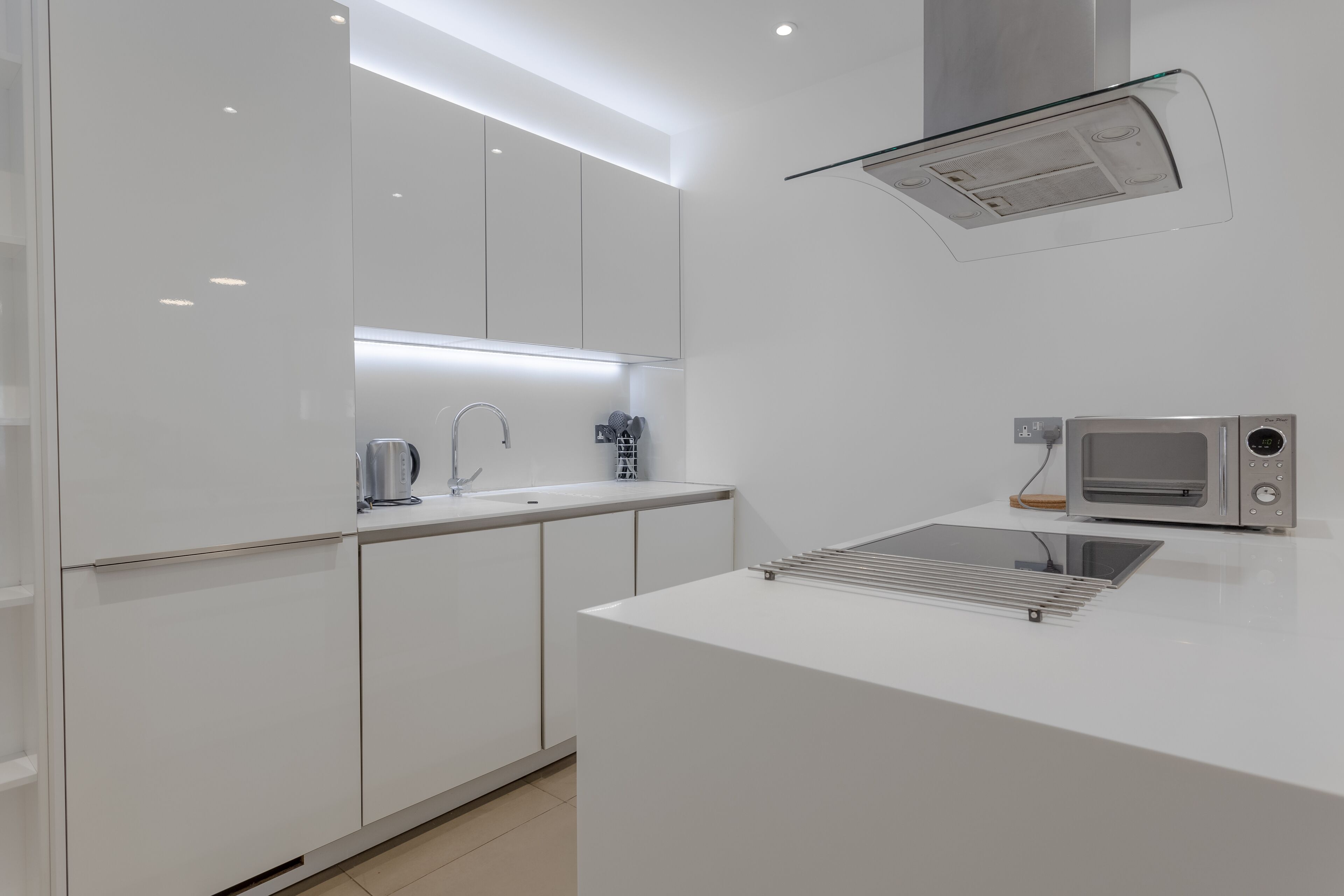 Een moderne keuken met witte kasten, een inbouwmagnetron en een roestvrijstalen spoelbak.