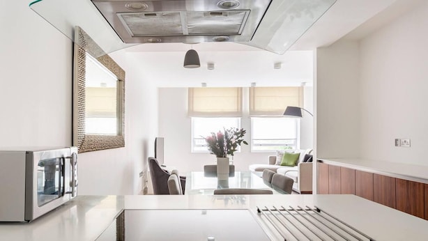 A modern kitchen with a built-in stove, a glass-top dining table, and a view into the living area. - Central London - 2 Beds - Sleeps 4 - Lift (London)