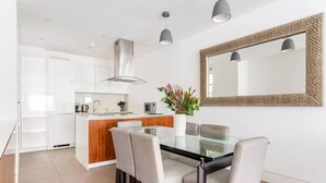 A modern kitchen with white cabinets, a wooden island, and a dining area with a glass table and grey upholstered chairs. - Central London - 2 Beds - Sleeps 4 - Lift (London)