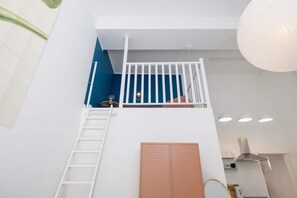 Stylish room with a staircase leading to a balcony and a small table with a lamp.