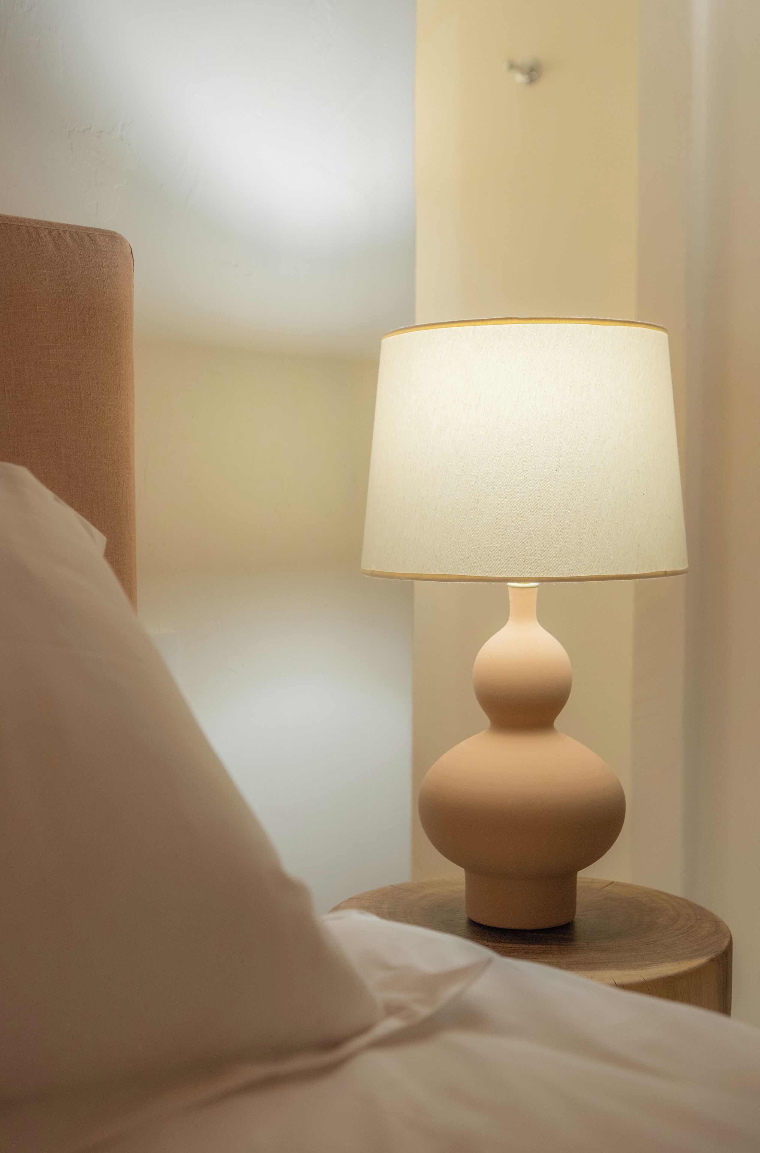 A bedside lamp on a wooden nightstand next to a bed with white bedding.