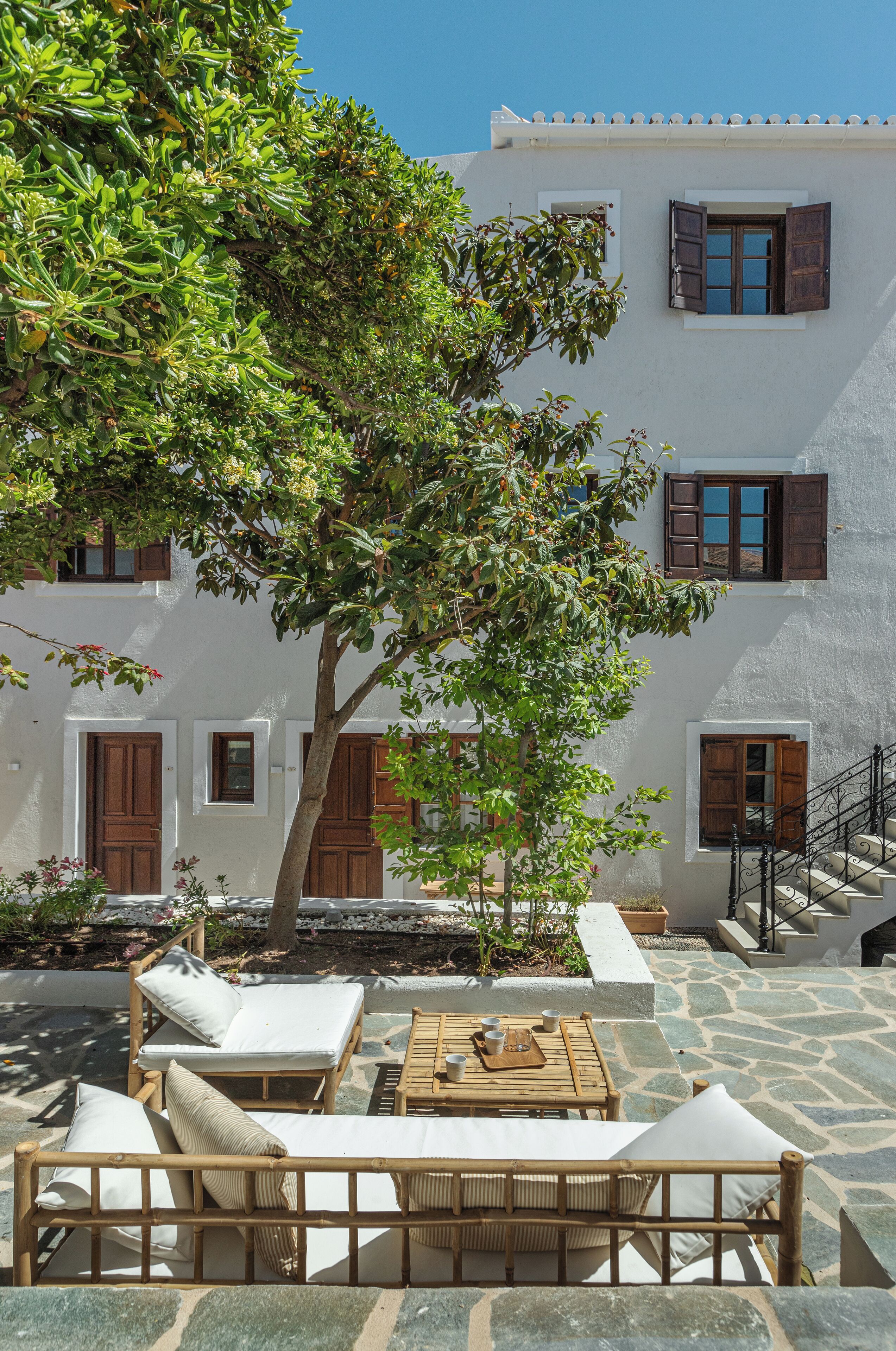 A courtyard with a white building, wooden furniture, and a tree.