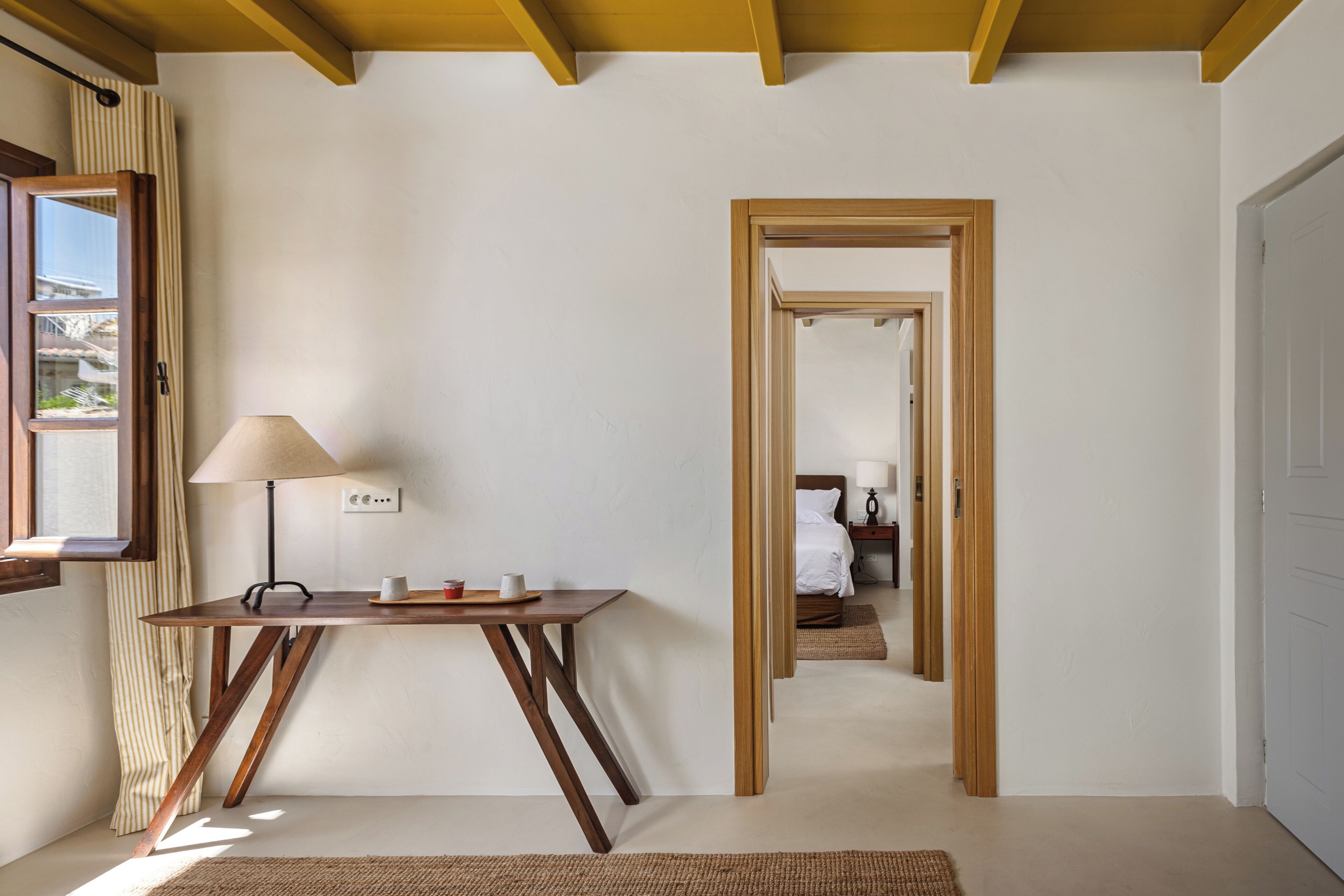 A room with a wooden desk, a lamp, and a window with curtains.