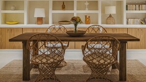 A dining area with a wooden table and wicker chairs, surrounded by white shelving with decorative items and books. - Teresa Spetses (Spetses)
