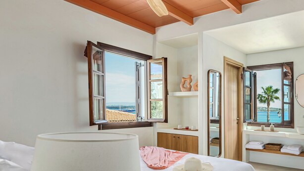 A bedroom with a bed, a bedside lamp, a view of the sea, and a ceiling fan. - Teresa Spetses (Spetses)